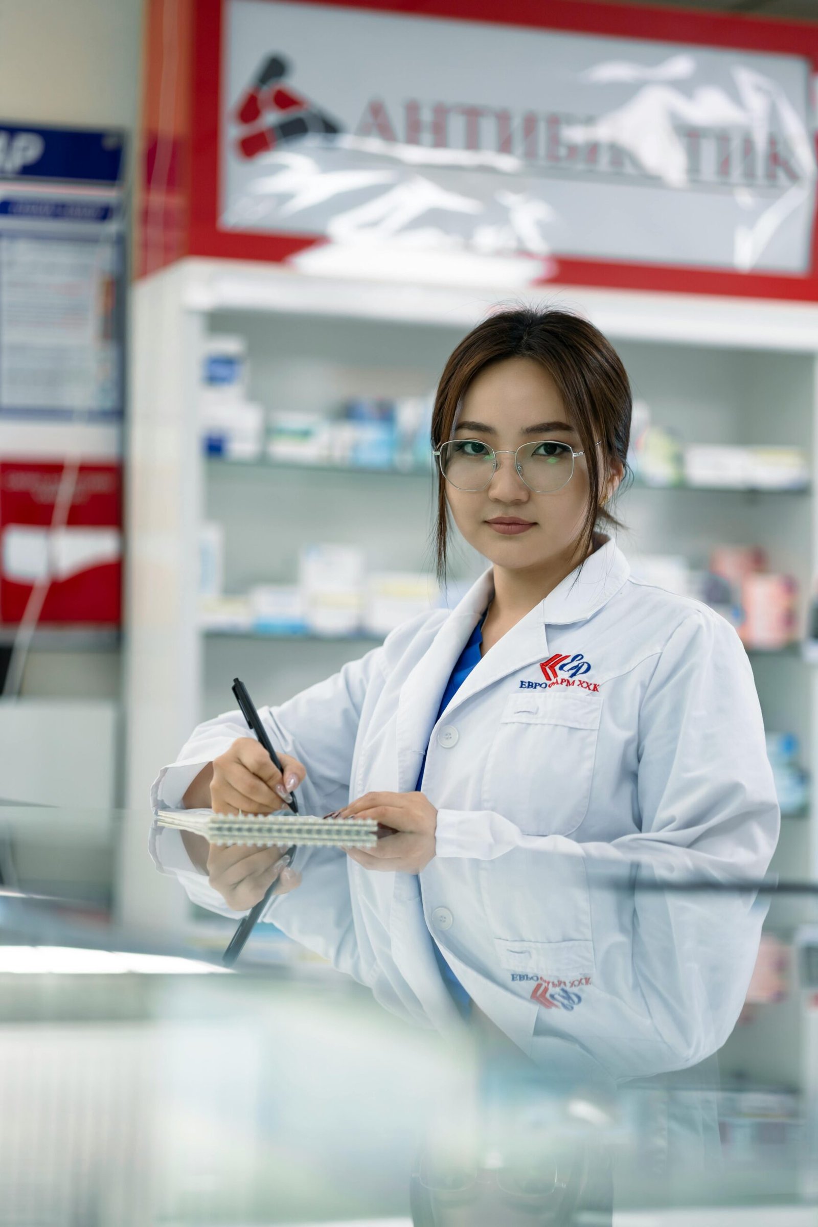 Female pharmacist writing in notepad inside a pharmacy.