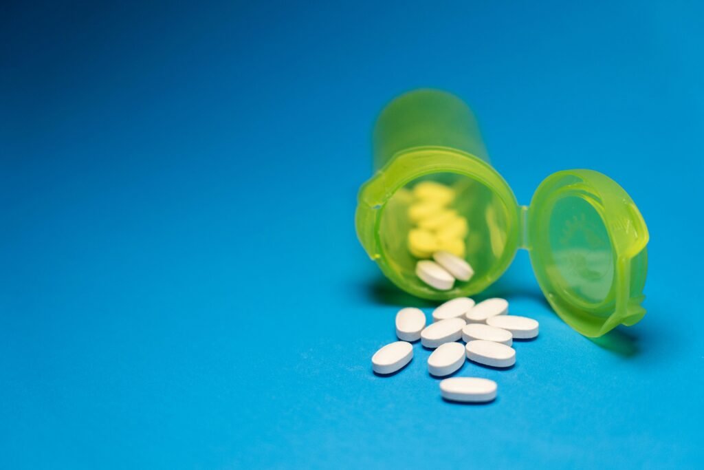 Image of a green pill bottle with white tablets scattered on a blue background, symbolizing healthcare and medication.