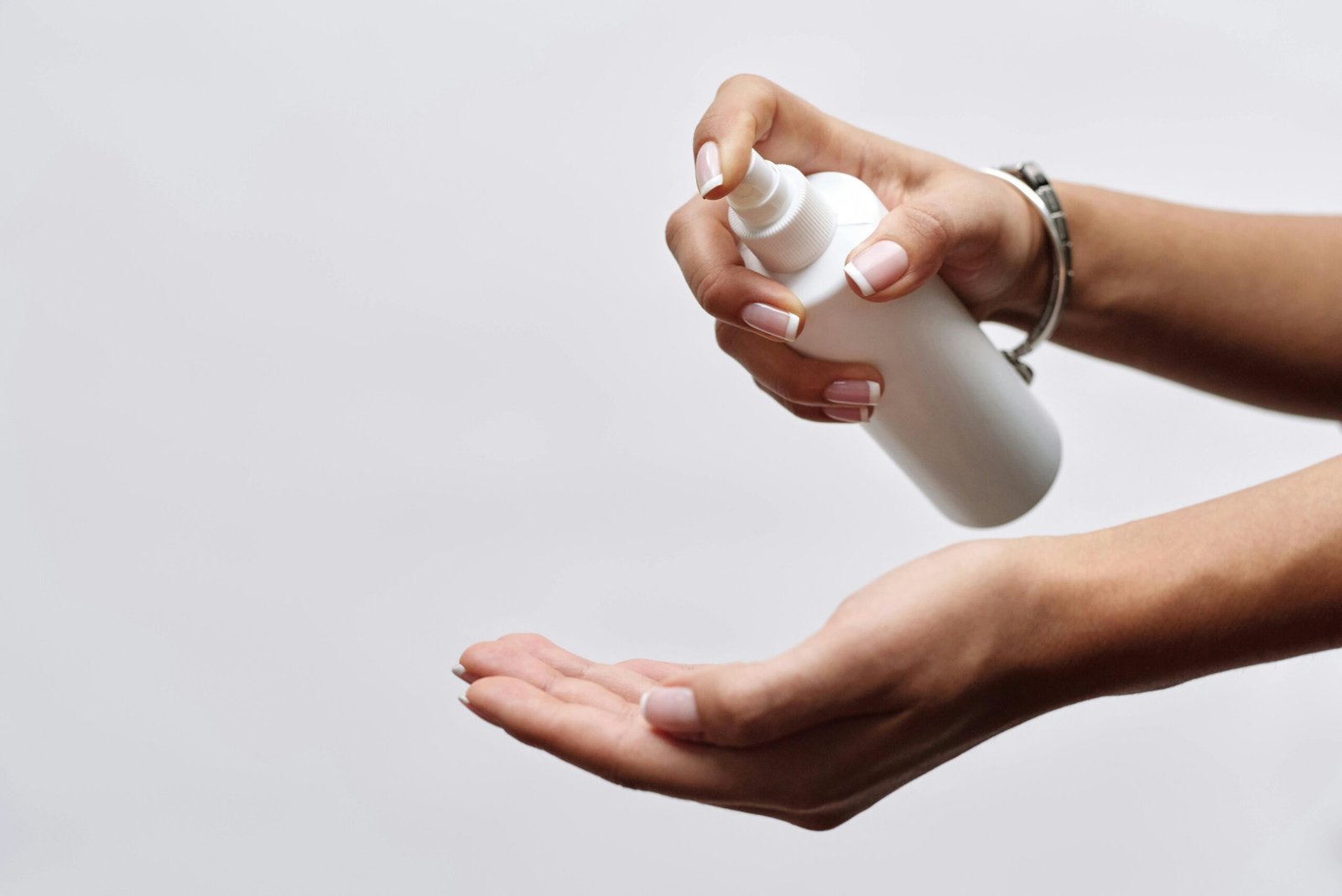 Close-up of hands applying sanitizer from a white spray bottle, showing hygiene care.
